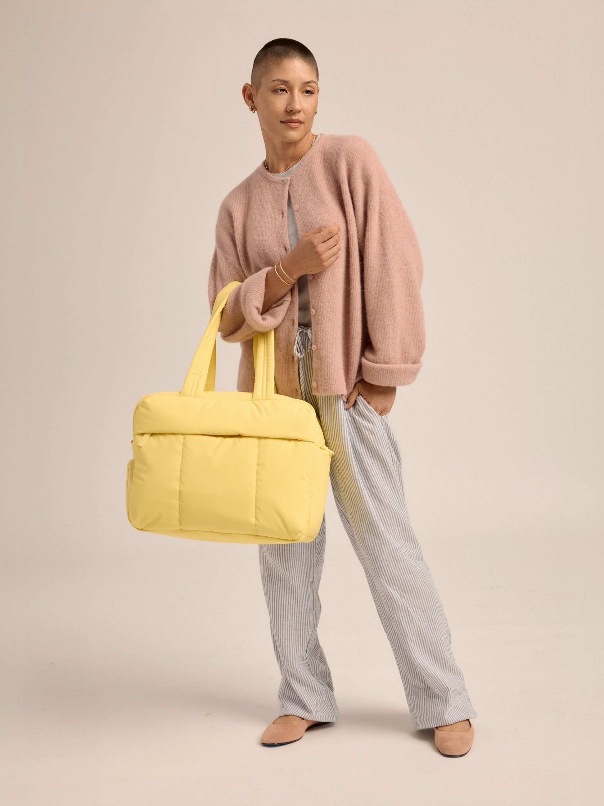 Model standing with yellow CALPAK Luka Duffel handle strap over arm;  DSM1901-BUTTER