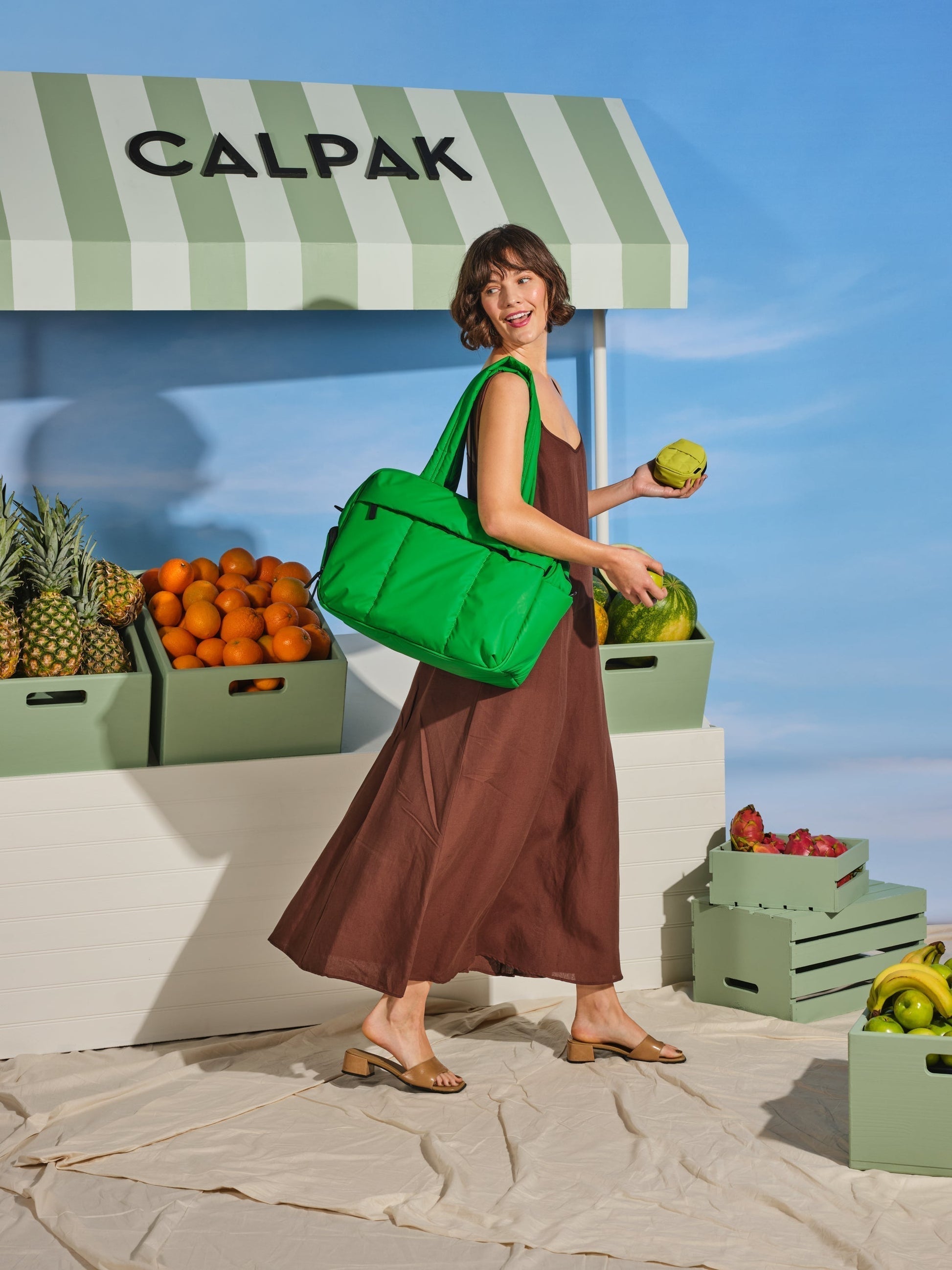 Model carrying CALPAK Luka Duffel Bag with dual straps and front zippered pocket  in green apple; DSM1901-GREEN-APPLE