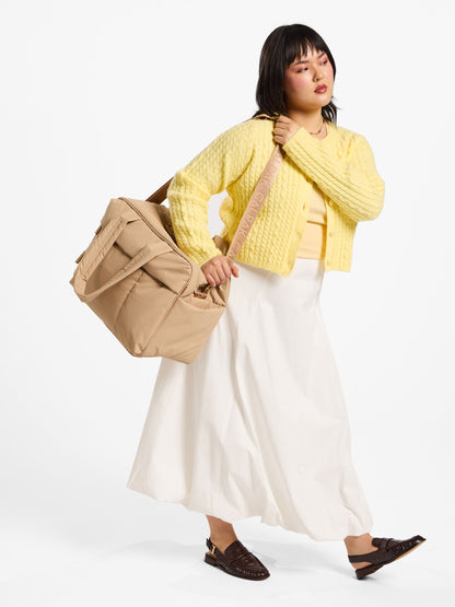 Model using removable strap of CALPAK luka duffel over shoulder in latte; DSM1901-LATTE
