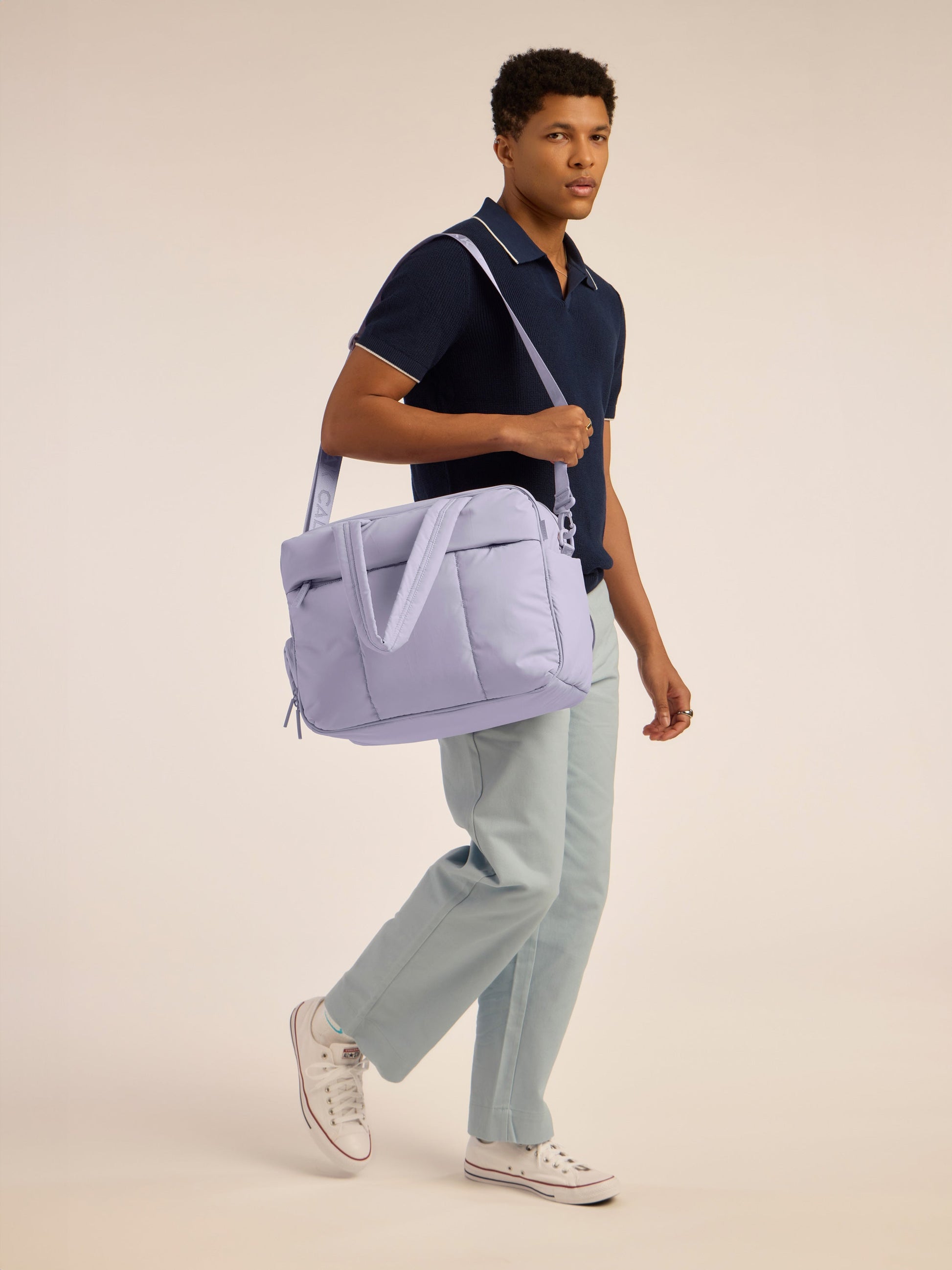 Male model holding CALPAK Luka Duffel monochrome in purple lavender Orchid by shoulder strap; DSM1901-ORCHID