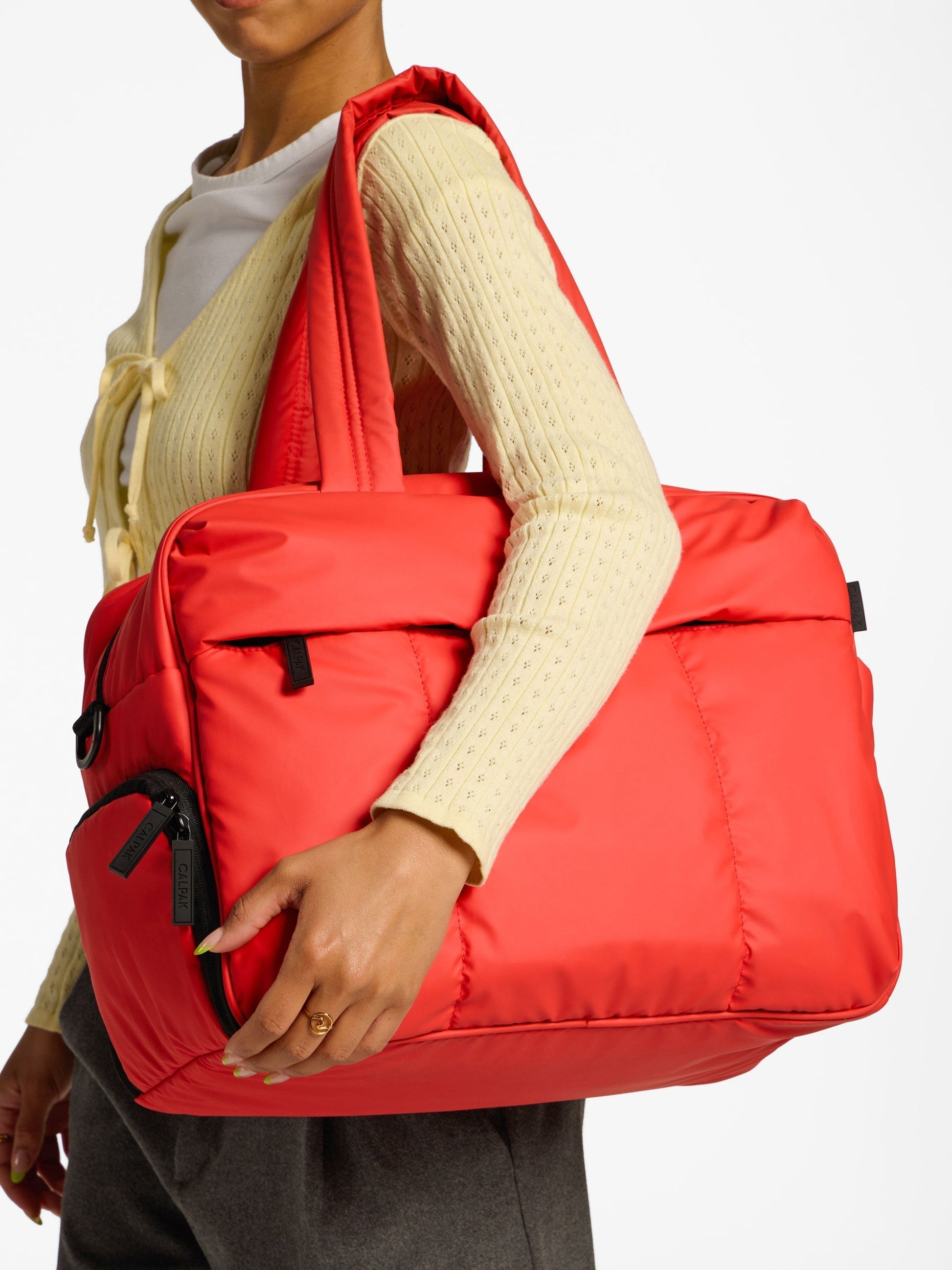 Model holding CALPAK Luka Duffel Bag over shoulder by handle in rouge; DSM1901-ROUGE