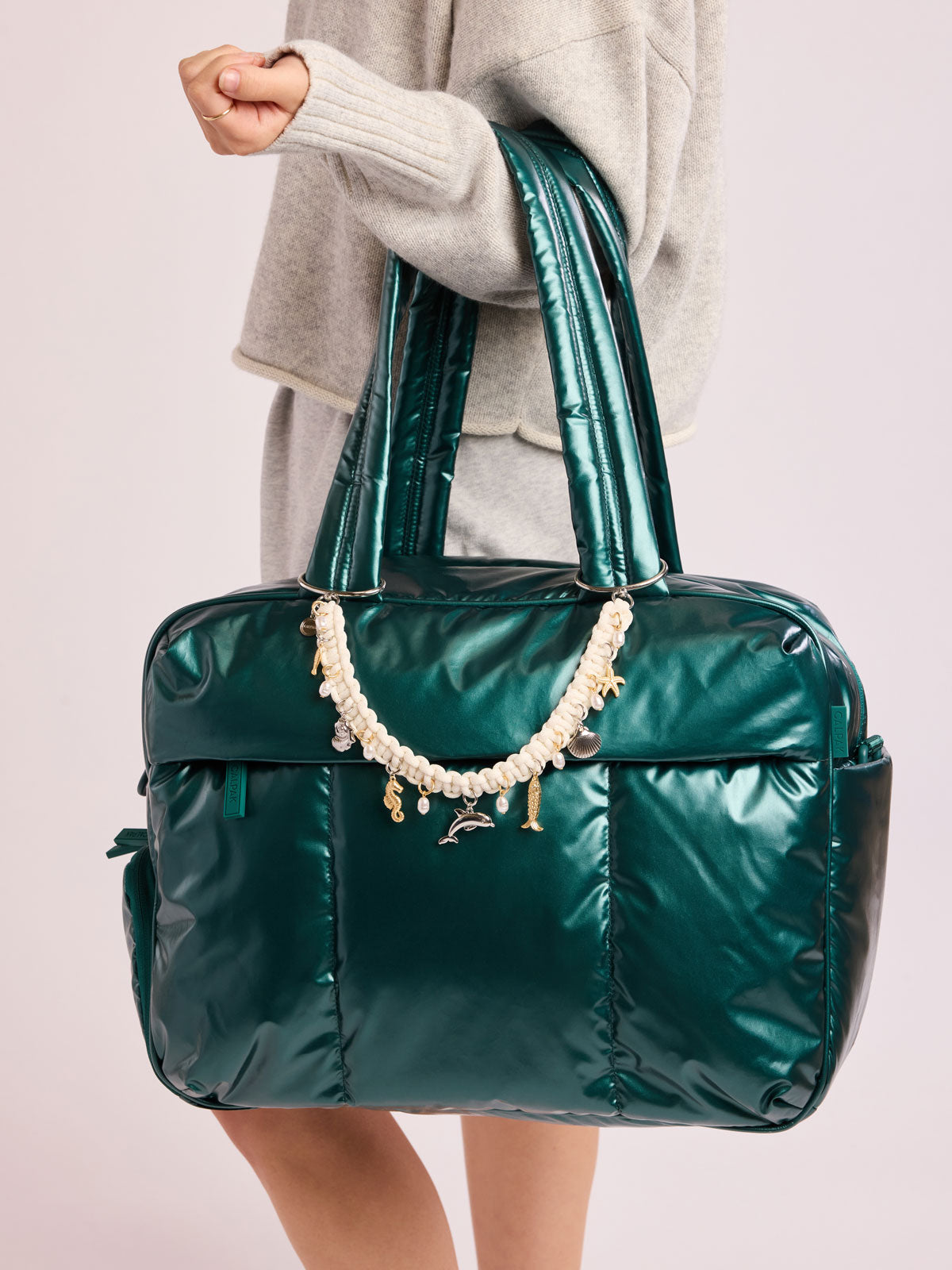 Woman carrying CALPAK  Luka Duffel in dark green shiny Glazed Kale with rope charm; DSM1901-GLAZED-KALE