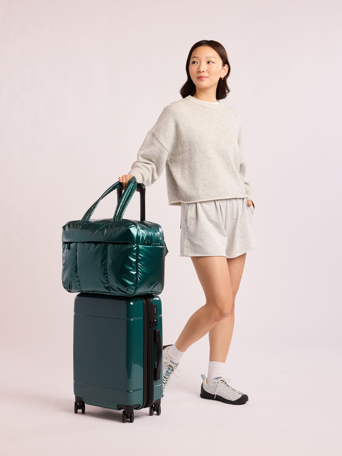 Woman with CALPAK  Luka Duffel in dark green shiny Glazed Kale on luggage ; DSM1901-GLAZED-KALE