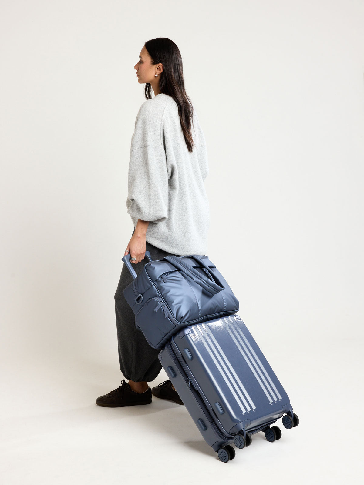 Woman carrying CALPAK Luka Duffel in metallic dark blue material Metallic Indigo; DSM1901-METALLIC-INDIGO