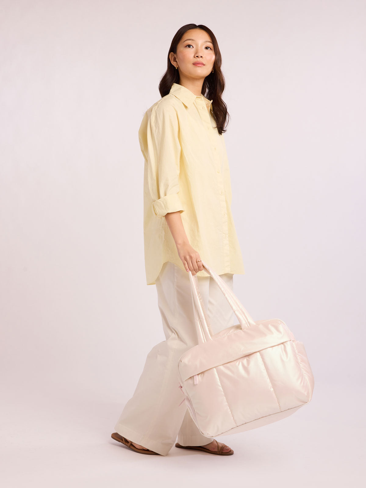 Woman holding CALPAK Luka Duffel in light pink shiny Pearlescent; DSM1901-PEARLESCENT