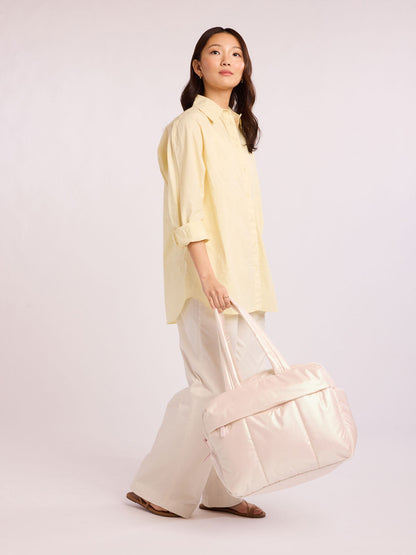Woman holding CALPAK Luka Duffel in light pink shiny Pearlescent; DSM1901-PEARLESCENT