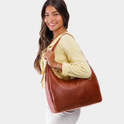 Nutmeg*Large | Model holding u-shaped, flat-bottomed leather shoulder bag with adjustable strap