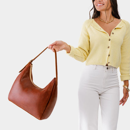 Nutmeg*Large | Model holding u-shaped, flat-bottomed leather shoulder bag with adjustable strap