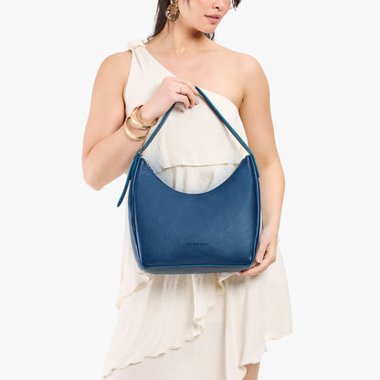 Caspian*Medium | Model holding u-shaped, flat-bottomed leather shoulder bag with adjustable strap