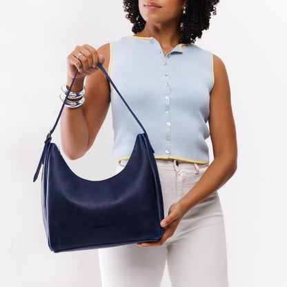 Cobalt*Medium | Model holding u-shaped, flat-bottomed leather shoulder bag with adjustable strap