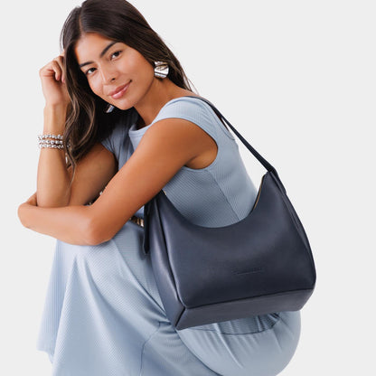 Night Owl*Medium | Model holding u-shaped, flat-bottomed leather shoulder bag with adjustable strap