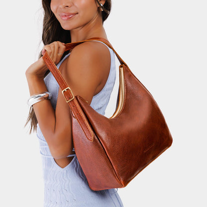 Nutmeg*Medium | Model holding u-shaped, flat-bottomed leather shoulder bag with adjustable strap