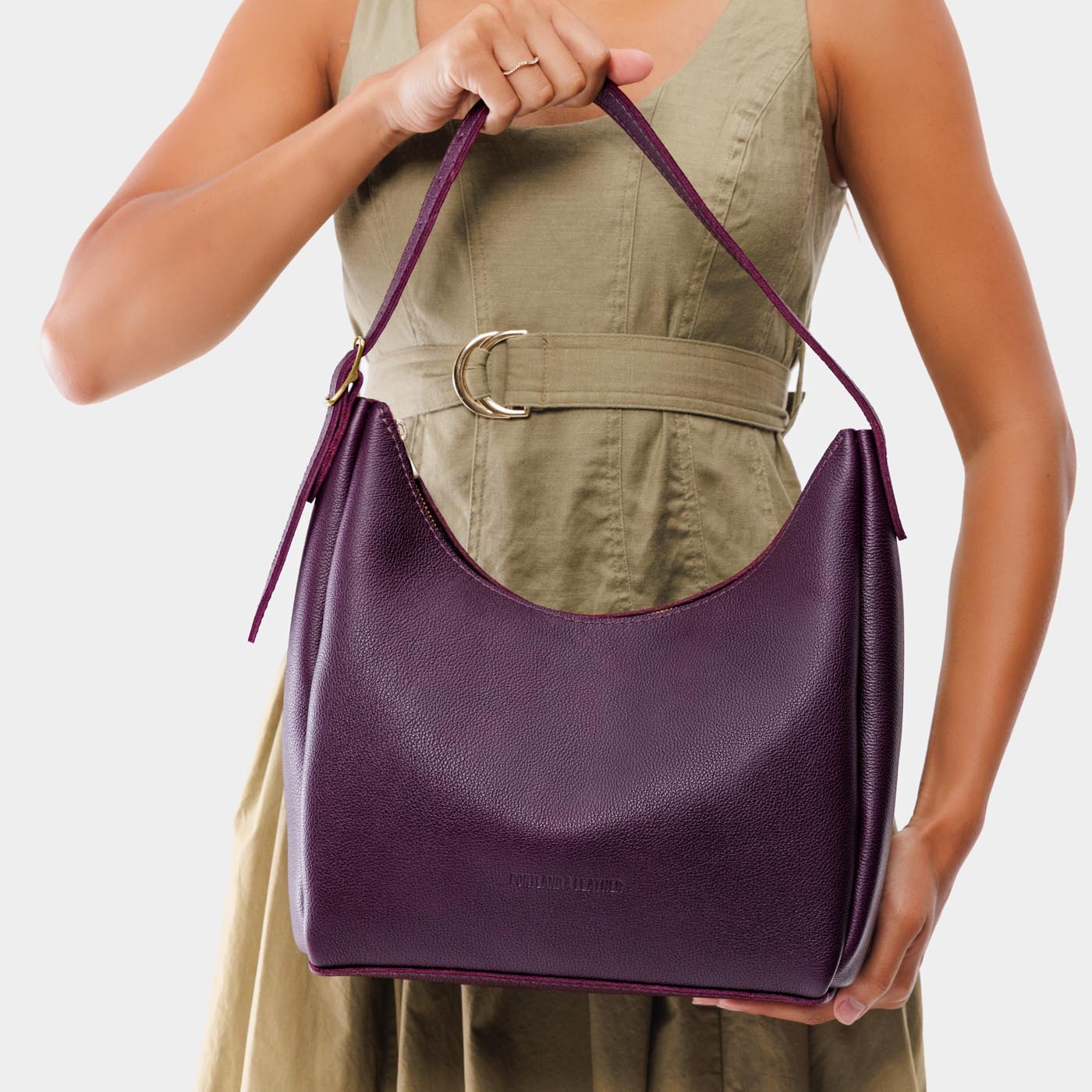 Plum*Medium | Model holding u-shaped, flat-bottomed leather shoulder bag with adjustable strap