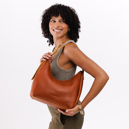 Sienna*Medium | Model holding u-shaped, flat-bottomed leather shoulder bag with adjustable strap